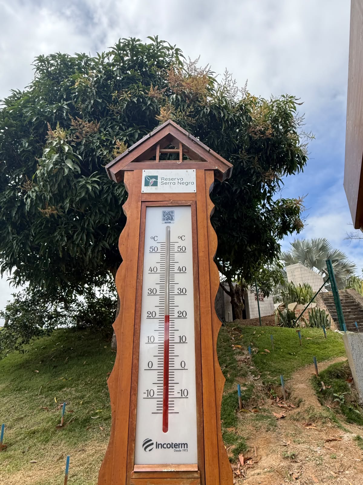 Termômetro de madeira com a placa do Condomínio Reserva Serra Negra, cercado de vegetação