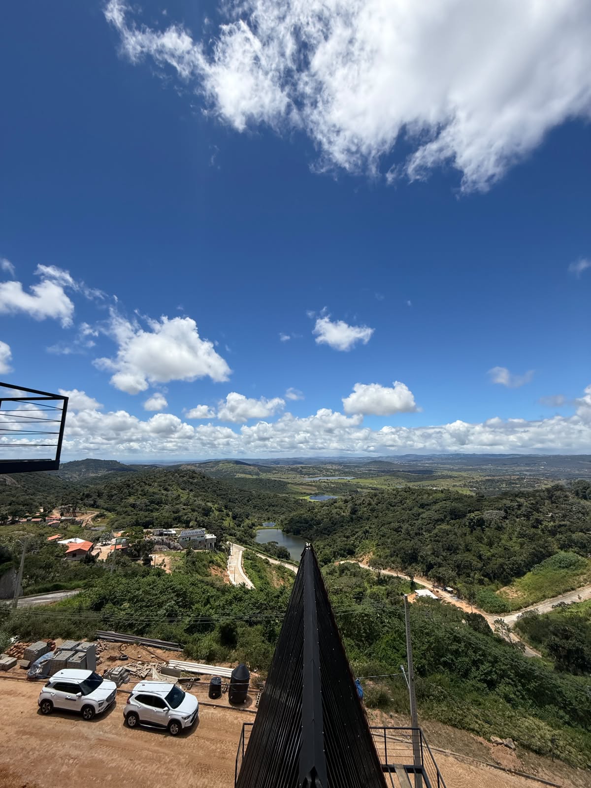 Cumeeira de uma cabana A-frame em obra, com o vale e o açude ao fundo (outubro de 2026)
